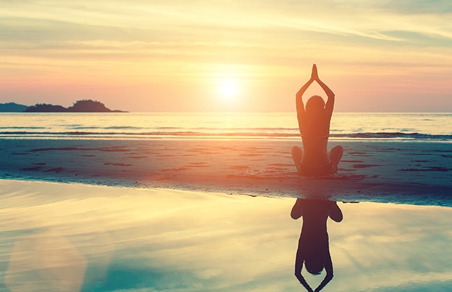 person meditating on the beach at sunrise